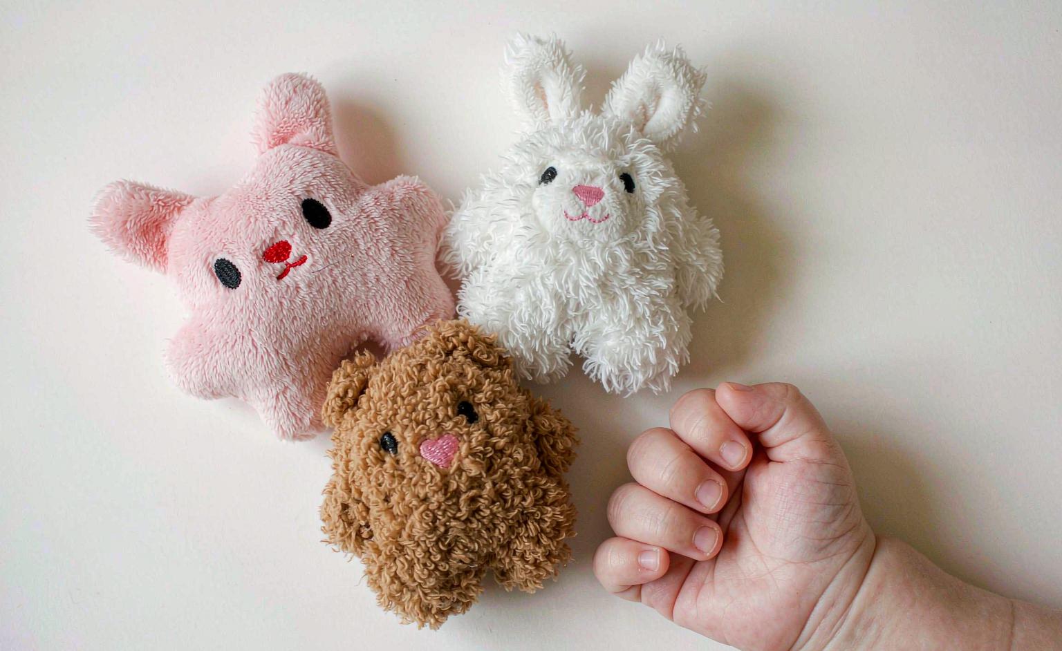A size comparison of plush toys beside a newborn's hand to show appropriate scale