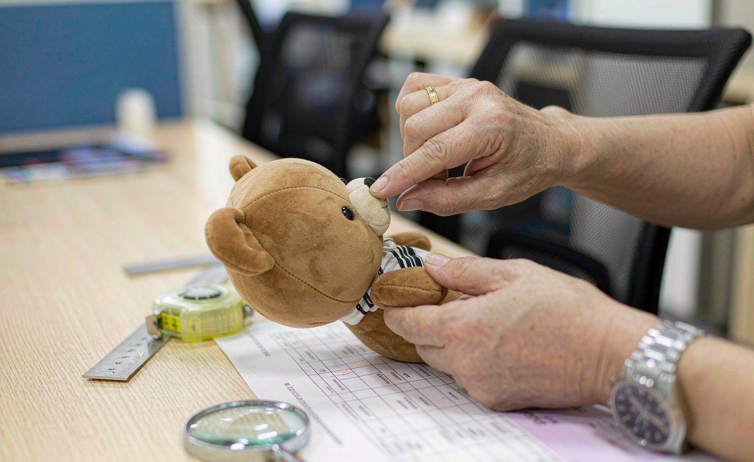 A buyer inspecting a plush toy sample against a printed approval checklist on a desk