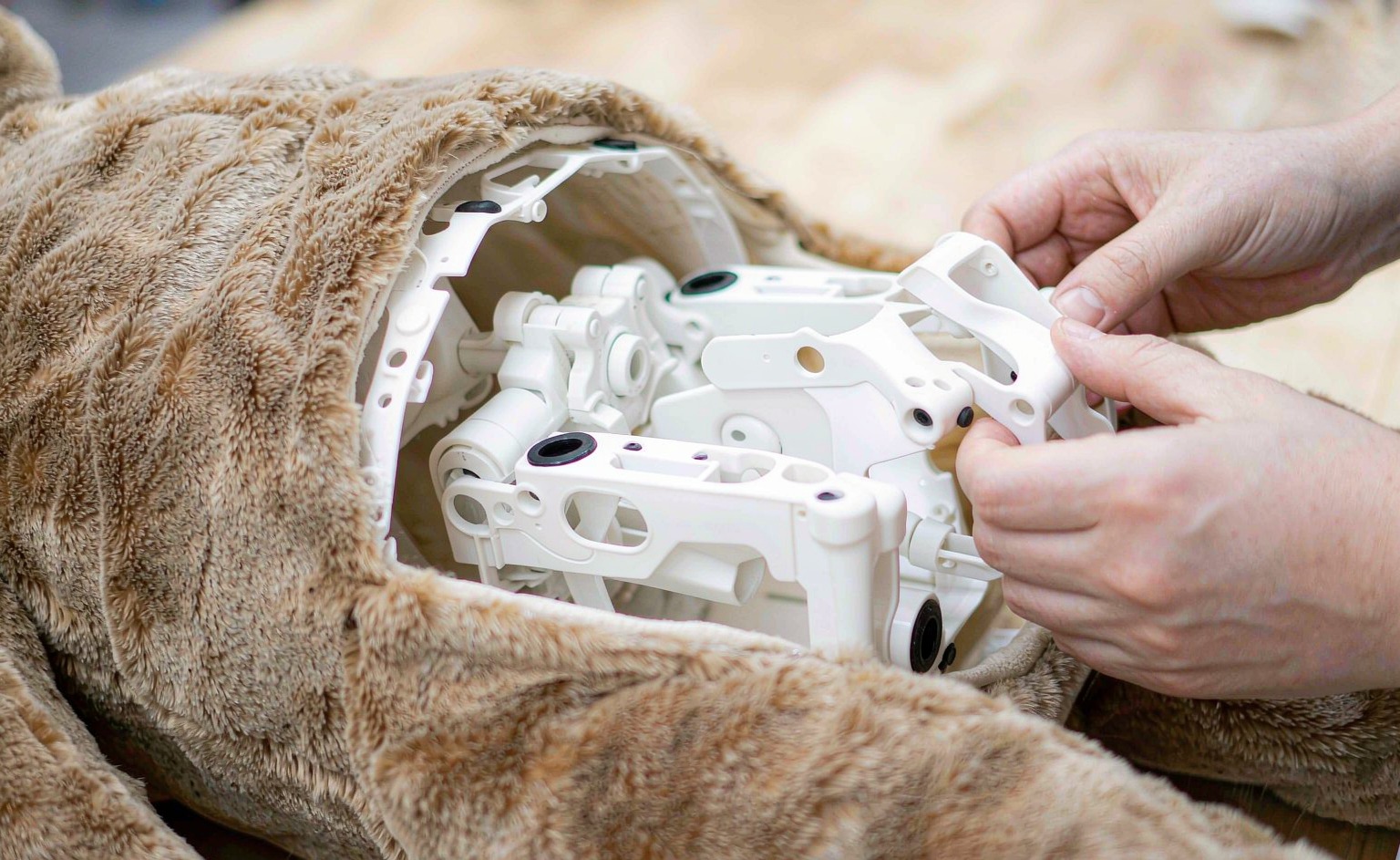 A plastic skeleton frame being positioned inside an unfinished plush toy body before stuffing