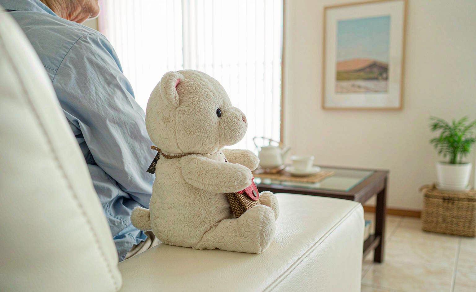 A plush toy resting on a senior's lap in a bright living room, symbolizing companionship