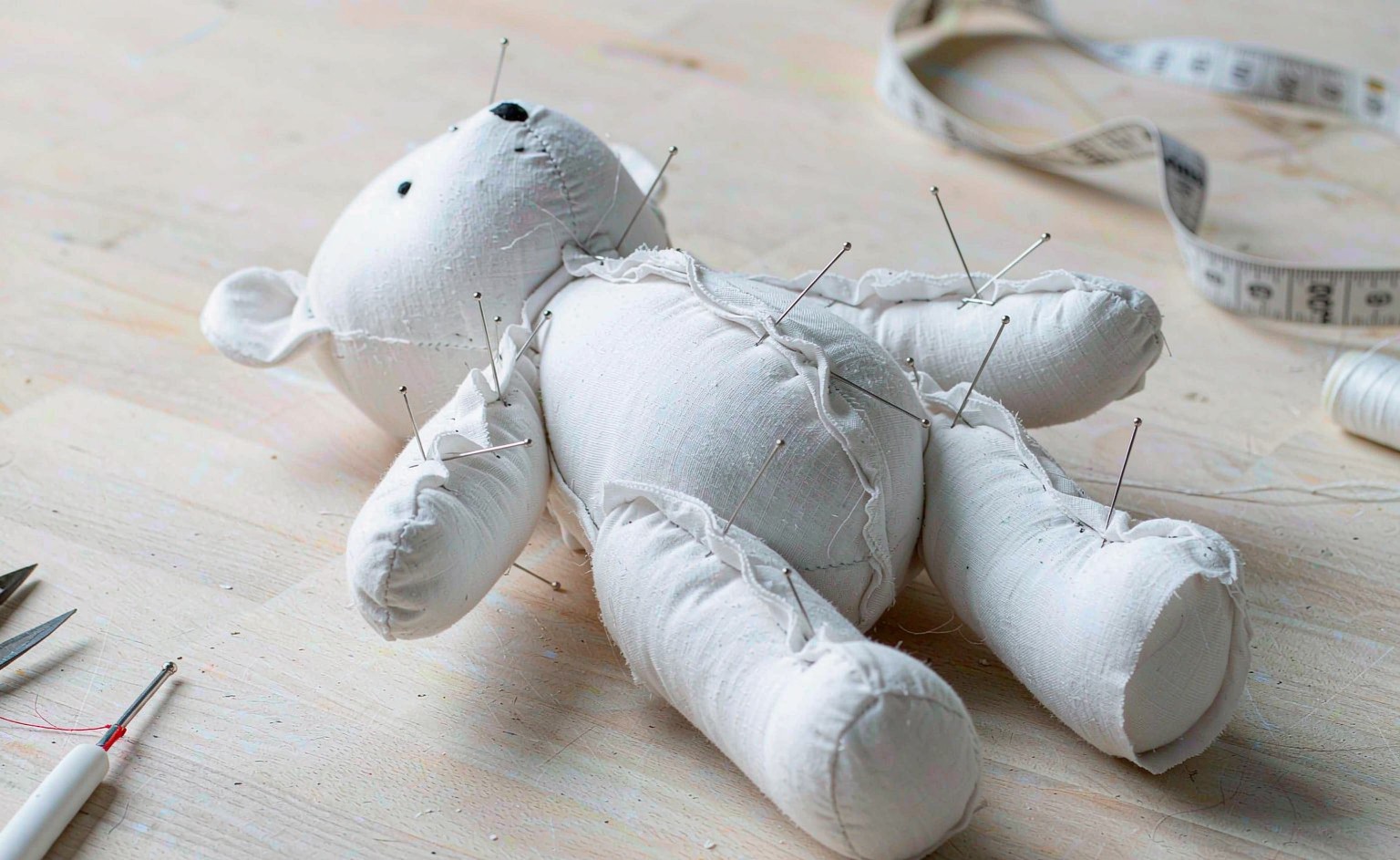 Close-up of an unstuffed white muslin plush toy body sample (white-body sample) pinned together on a workbench, showing the raw silhouette before fabric and embroidery are applied