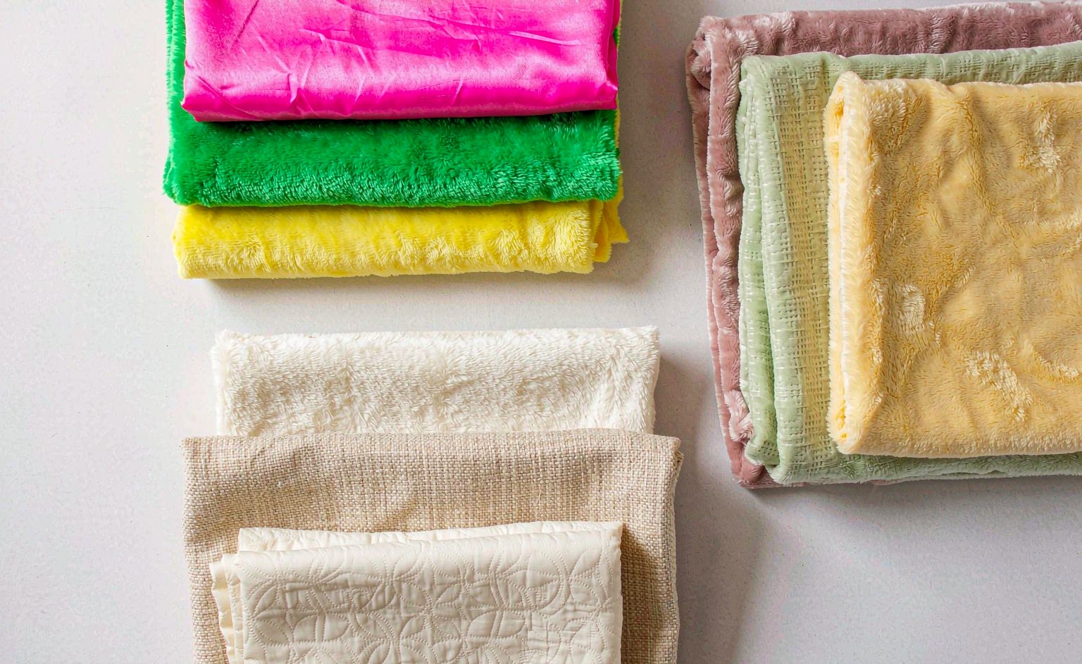 A color palette flat-lay photograph showing three groups of plush fabric swatches for Easter 2027: bright classic pastels in hot pink and kelly green, muted design-forward pastels in dusty rose and sage, and warm neutral creams and oatmeals, arranged on a light background