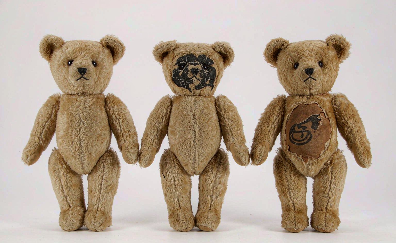A detailed comparison photograph showing three identical plush bear samples side by side after wash testing: one with crisp embroidered facial features intact, one with a cracked and faded screen-printed face, and one with a peeled heat-transfer logo showing edge lifting